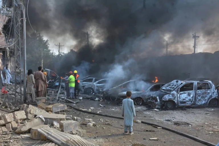 Rescue workers and paramilitary soldiers working through smoke and wreckage at the site of the BLA suicide bombing in Quetta on May 24, 2026 — a vehicle-borne explosion derailed a train carrying military personnel home for Eid ul-Adha, killing at least 23 people