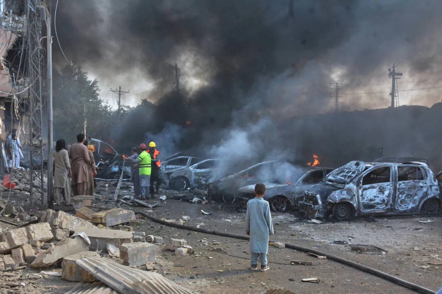 Rescue workers and paramilitary soldiers working through smoke and wreckage at the site of the BLA suicide bombing in Quetta on May 24, 2026 — a vehicle-borne explosion derailed a train carrying military personnel home for Eid ul-Adha, killing at least 23 people